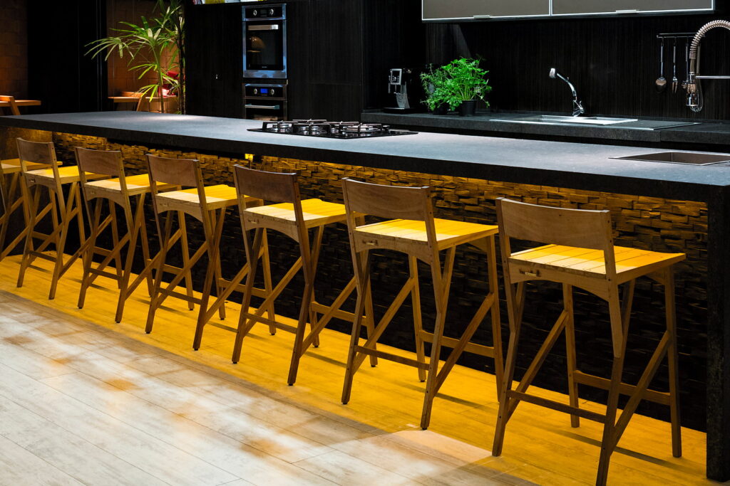 Bancada principal do Amazônia Gourmet com as banquetas amarelas alinhadas, cooktop e cuba embutidos na pedra