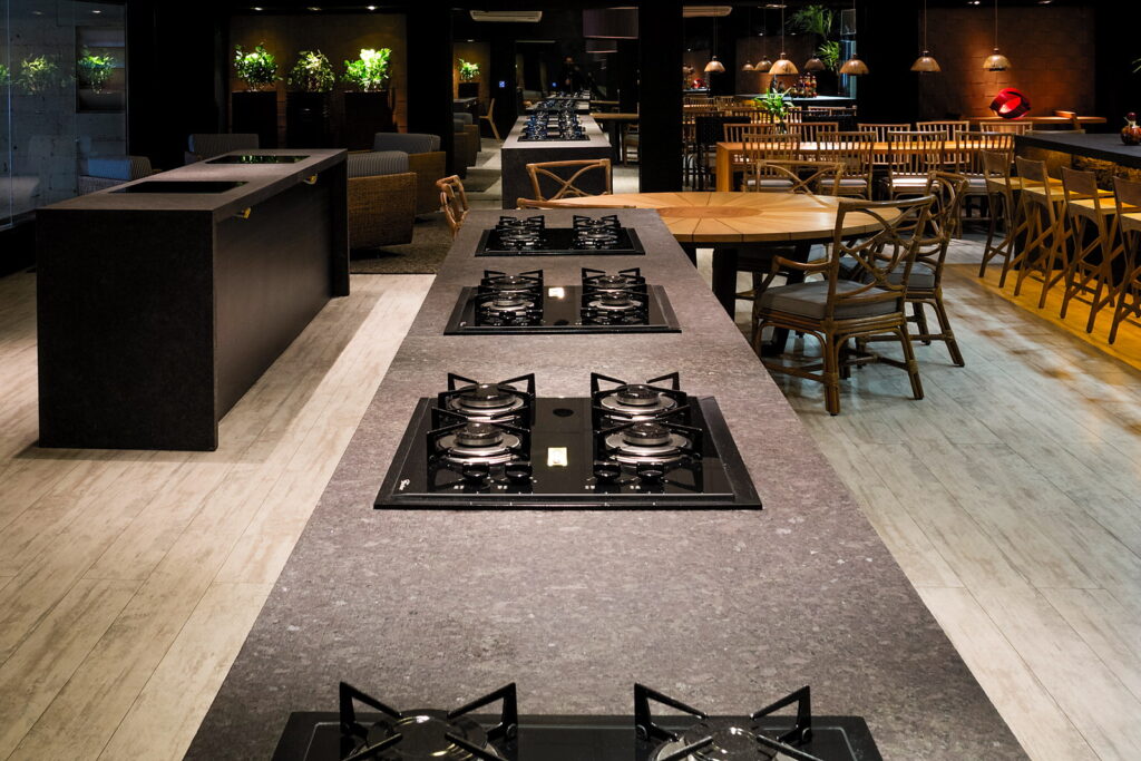 Bancadas de trabalho do Amazônia Gourmet com os cooktops individuais alinhados e a mesa comunitária ao fundo
