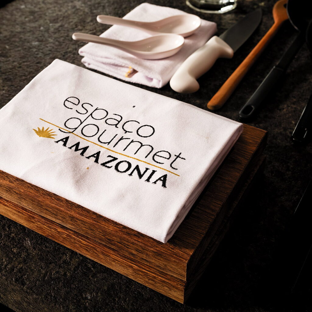 Pano com a marca Espaço Gourmet Amazônia sobre a tábua, ao lado dos utensílios de serviço