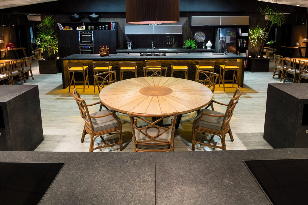 Vista ampla do salão do Amazônia Gourmet, com a mesa redonda ao centro, a bancada de cocção ao fundo e as bancadas de trabalho nas laterais