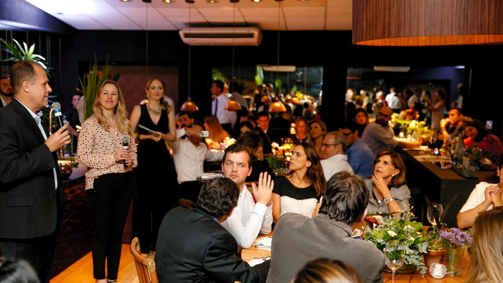 Salão do Amazônia Gourmet cheio durante evento corporativo, com apresentação ao microfone e convidados jantando nas mesas