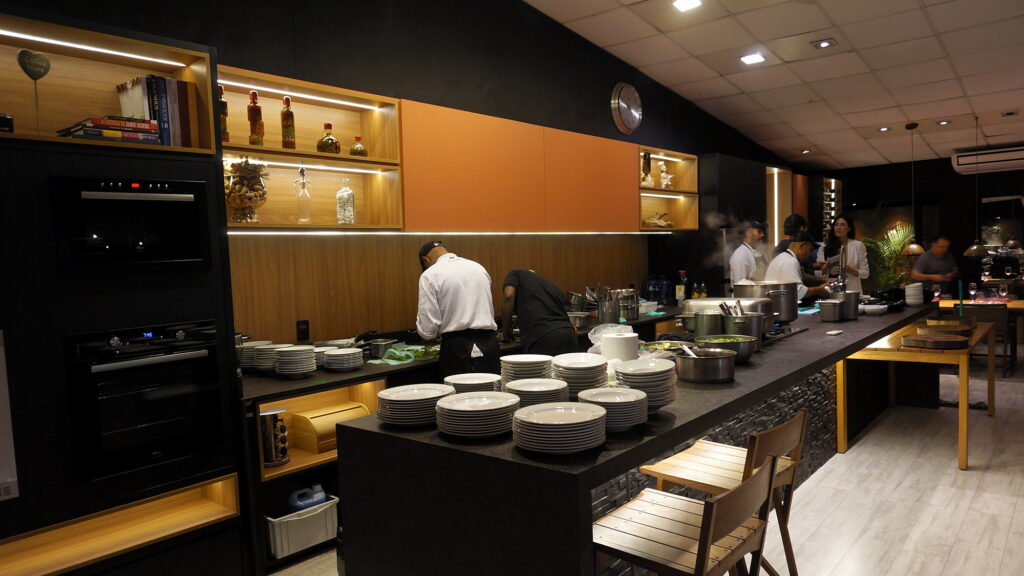 Cozinha do Amazônia Gourmet em operação, com a equipe trabalhando atrás da bancada principal e a louça do serviço empilhada