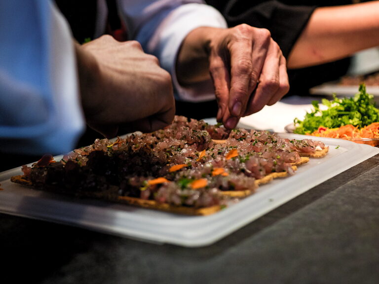 Participante e cozinheiro finalizam juntos a travessa do menu durante team building gastronômico